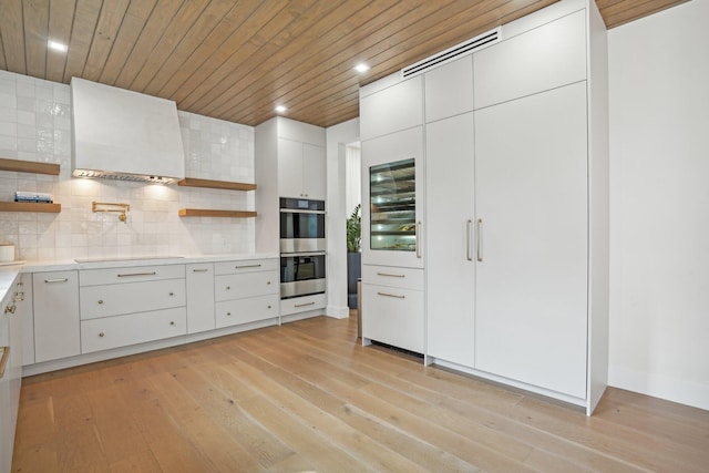 kitchen featuring stainless steel double oven, white cabinets, light hardwood / wood-style flooring, and beverage cooler