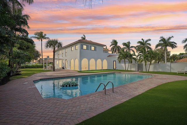 pool at dusk with a patio and a lawn