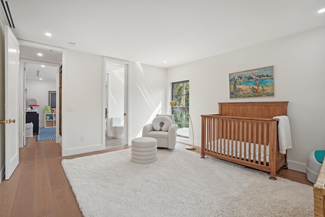 bedroom featuring hardwood / wood-style flooring, a crib, and connected bathroom