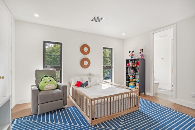 bedroom featuring connected bathroom, hardwood / wood-style flooring, and multiple windows