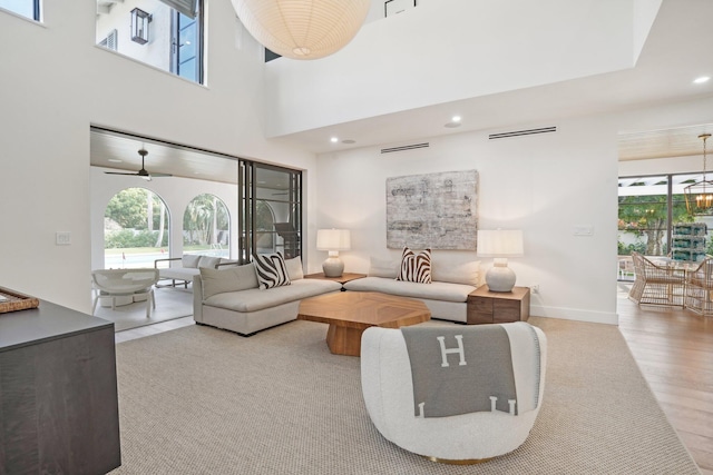 living room with light hardwood / wood-style flooring, a wealth of natural light, a high ceiling, and ceiling fan