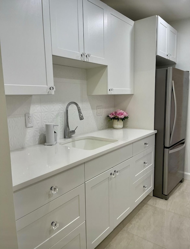 kitchen featuring decorative backsplash, stainless steel fridge, white cabinetry, and sink