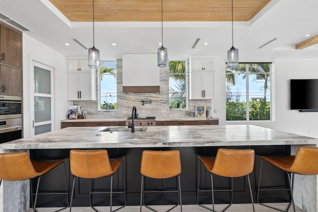 kitchen featuring decorative backsplash, white cabinets, and a large island with sink