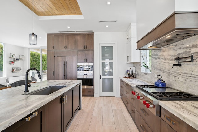 kitchen with sink, pendant lighting, premium range hood, appliances with stainless steel finishes, and tasteful backsplash