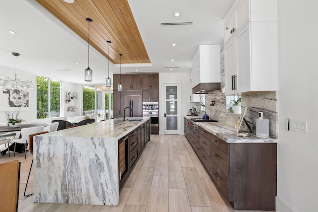 kitchen with sink, dark brown cabinets, pendant lighting, white cabinets, and light hardwood / wood-style flooring