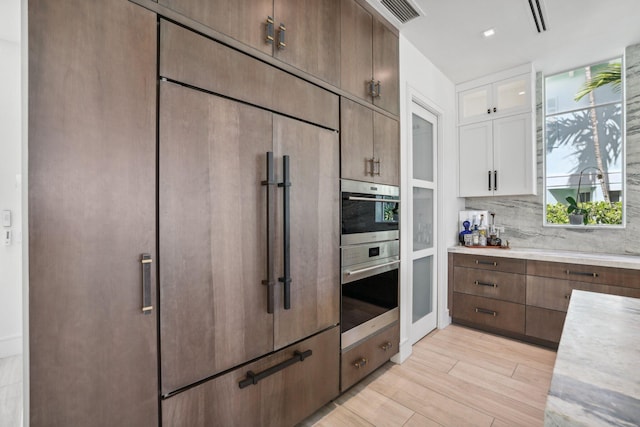 kitchen with backsplash, white cabinets, paneled refrigerator, and light hardwood / wood-style floors