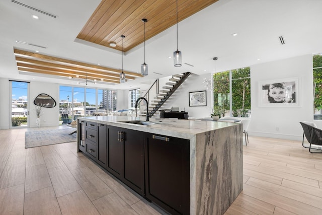 kitchen with light stone countertops, a kitchen island with sink, pendant lighting, and light wood-type flooring