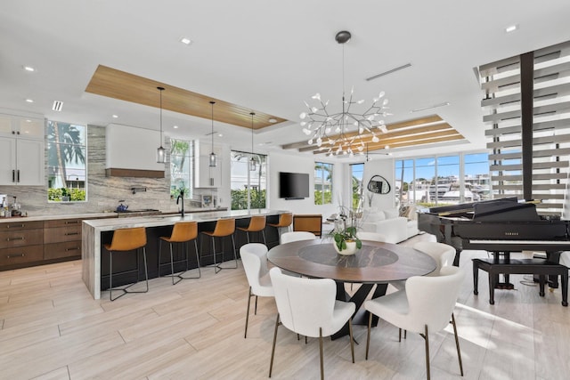 dining room with a notable chandelier, sink, a tray ceiling, and light wood-type flooring