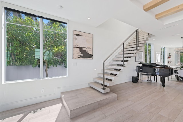 staircase with beam ceiling, a chandelier, and hardwood / wood-style floors