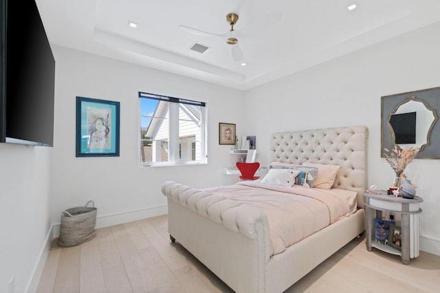 bedroom with light hardwood / wood-style floors, a tray ceiling, and ceiling fan