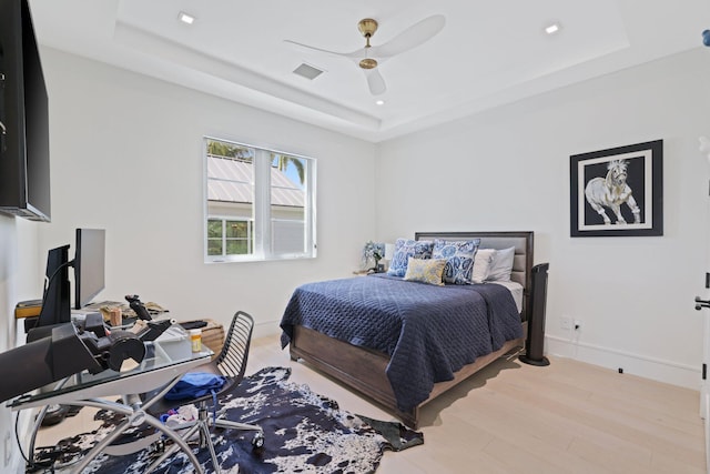 bedroom with a raised ceiling, light hardwood / wood-style floors, and ceiling fan