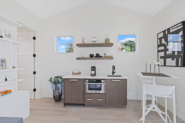 bar with light wood-type flooring, stainless steel oven, vaulted ceiling, and a wealth of natural light