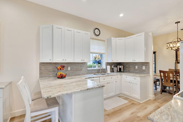 kitchen with kitchen peninsula, white cabinetry, sink, and decorative light fixtures