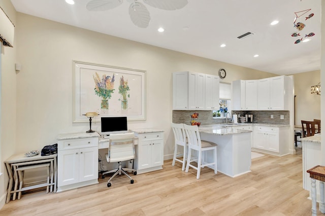 kitchen featuring kitchen peninsula, a kitchen breakfast bar, ceiling fan, white cabinets, and light hardwood / wood-style floors