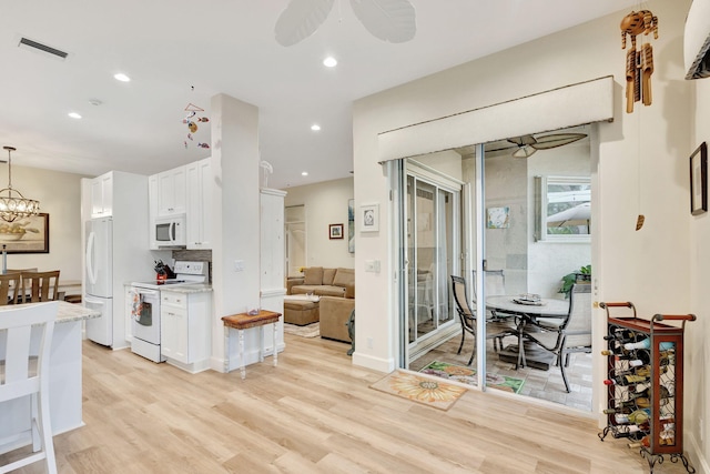 kitchen with white appliances, white cabinets, ceiling fan with notable chandelier, light hardwood / wood-style flooring, and decorative light fixtures