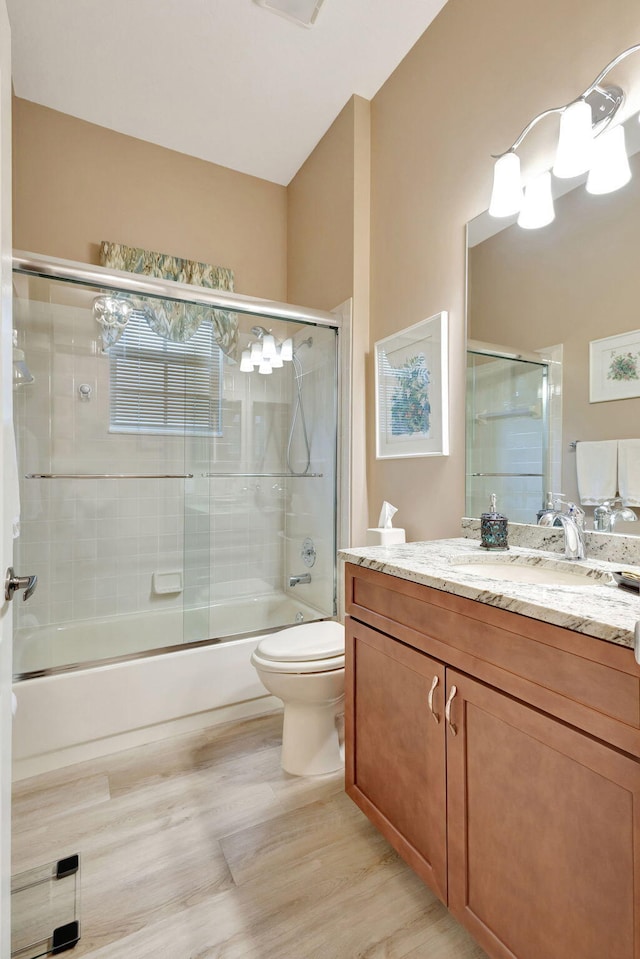 full bathroom with hardwood / wood-style flooring, vanity, enclosed tub / shower combo, and toilet