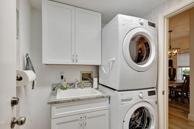 washroom featuring cabinets, light wood-type flooring, sink, stacked washer and clothes dryer, and a chandelier