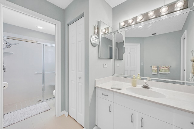 bathroom featuring toilet, vanity, tile patterned floors, and a shower with door