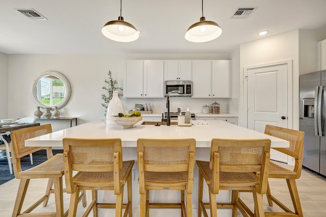 kitchen featuring a kitchen island with sink, white cabinetry, decorative light fixtures, and stainless steel appliances