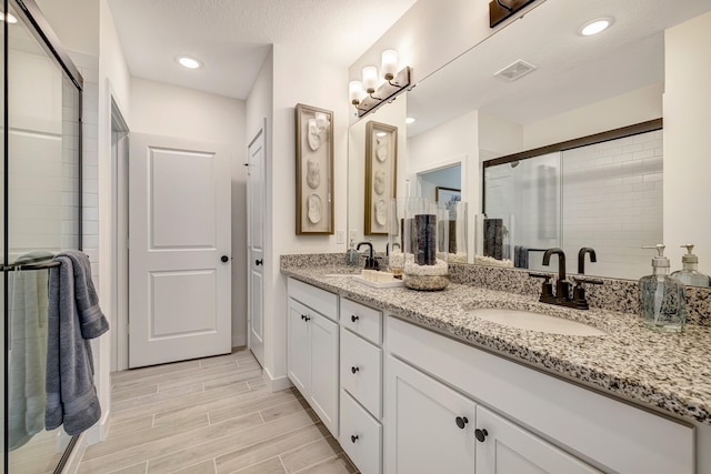 bathroom with vanity, a shower with shower door, and a textured ceiling