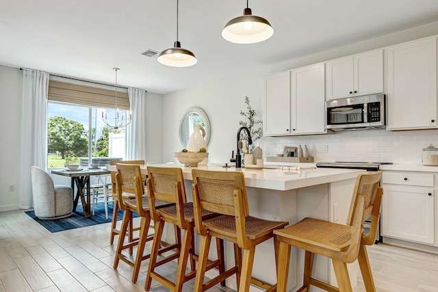 kitchen featuring white cabinets, decorative light fixtures, and a center island with sink