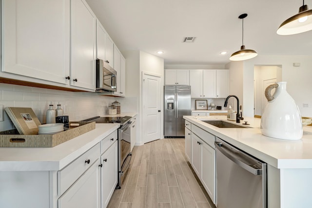 kitchen featuring white cabinets, hanging light fixtures, appliances with stainless steel finishes, light wood-type flooring, and sink