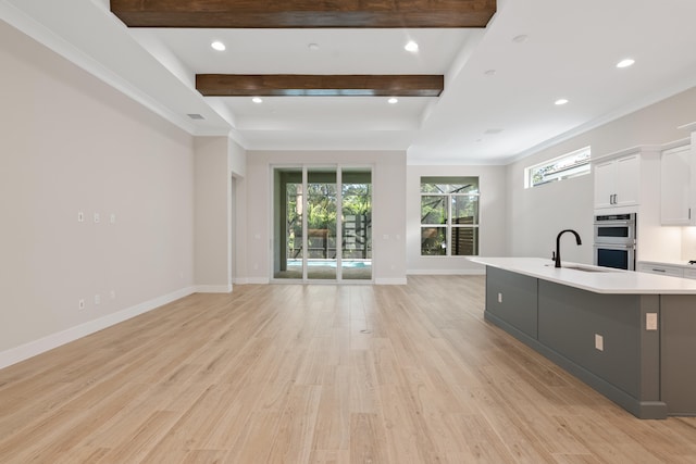 kitchen with sink, double oven, white cabinets, light hardwood / wood-style flooring, and a kitchen island with sink