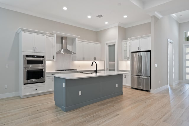 kitchen with appliances with stainless steel finishes, sink, white cabinetry, wall chimney exhaust hood, and a center island with sink