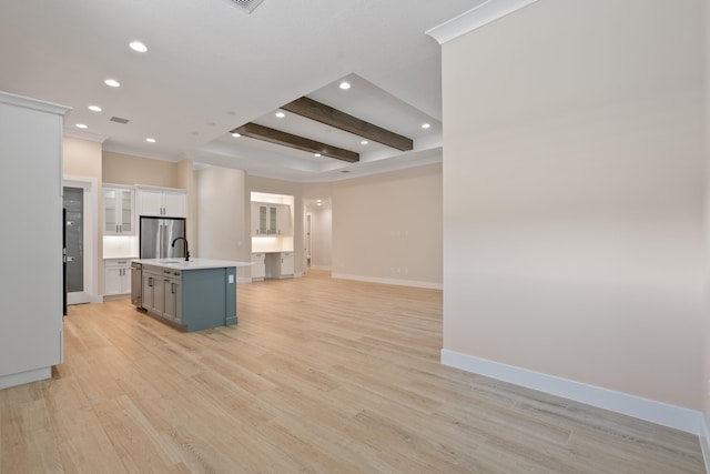 kitchen featuring beamed ceiling, an island with sink, white cabinets, light hardwood / wood-style floors, and stainless steel refrigerator