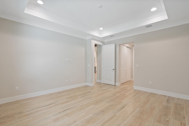 empty room with ornamental molding, a tray ceiling, and light wood-type flooring