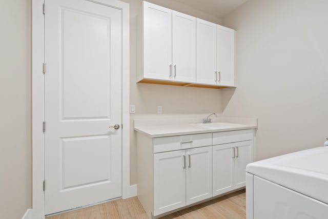 laundry room featuring sink, light hardwood / wood-style flooring, washer / clothes dryer, and cabinets