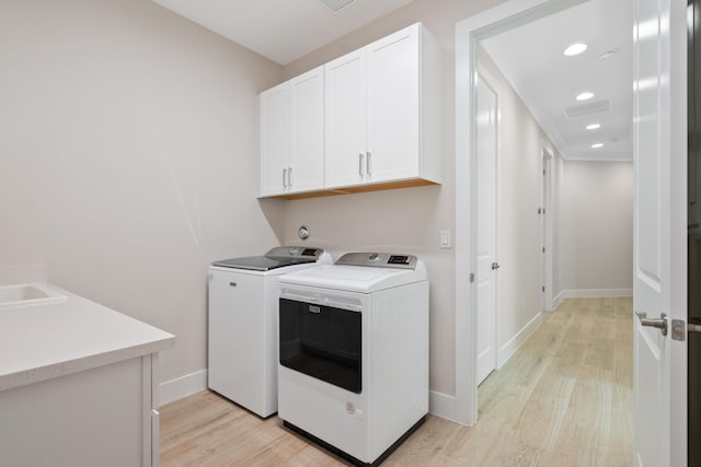 washroom with washer and dryer, cabinets, and light hardwood / wood-style flooring