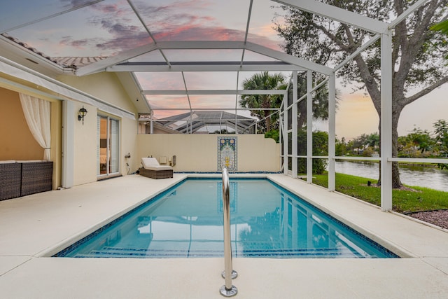 pool at dusk featuring a patio, a water view, and glass enclosure