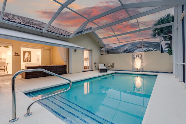 pool at dusk with a patio area and glass enclosure