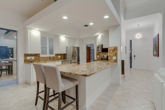 kitchen featuring hanging light fixtures, kitchen peninsula, stainless steel appliances, backsplash, and white cabinetry