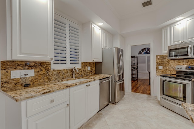 kitchen featuring decorative backsplash, appliances with stainless steel finishes, white cabinetry, light stone countertops, and sink