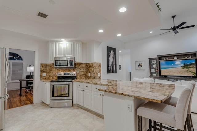 kitchen featuring appliances with stainless steel finishes, kitchen peninsula, white cabinets, light stone counters, and a breakfast bar area