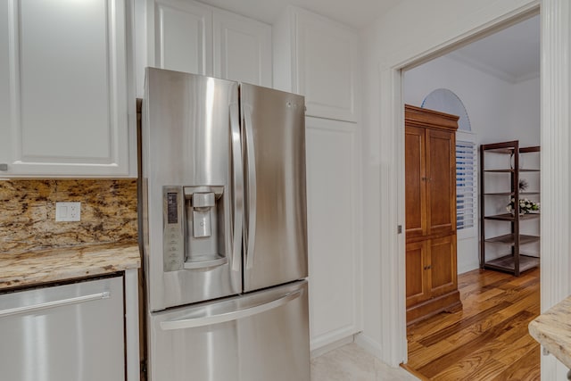 kitchen with white cabinets, appliances with stainless steel finishes, light stone countertops, light wood-type flooring, and crown molding