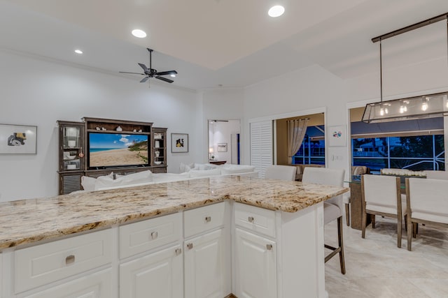 kitchen with ceiling fan, a kitchen breakfast bar, white cabinetry, light stone countertops, and pendant lighting