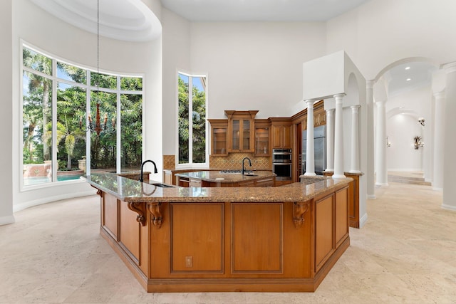 kitchen featuring a large island with sink, a sink, fridge, a high ceiling, and brown cabinets