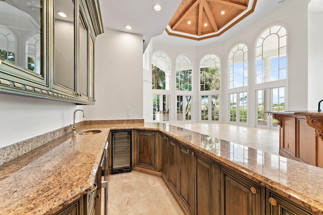 kitchen with recessed lighting, a towering ceiling, light stone counters, wine cooler, and a sink
