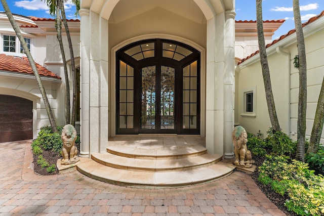 view of exterior entry featuring stucco siding, a garage, a tiled roof, and french doors