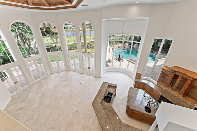 interior space featuring a water view, a towering ceiling, visible vents, coffered ceiling, and stone finish flooring