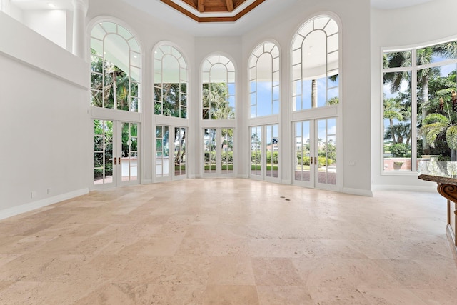 unfurnished living room featuring a high ceiling, a healthy amount of sunlight, stone tile floors, and baseboards