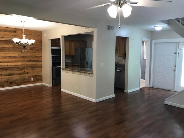 kitchen with dark wood-type flooring, wood walls, black appliances, and decorative backsplash