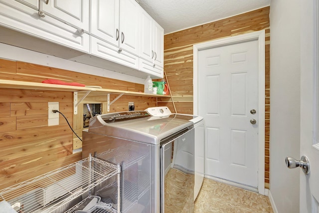 laundry room featuring a textured ceiling, cabinets, wooden walls, and washing machine and clothes dryer