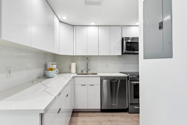 kitchen featuring white cabinetry, light stone countertops, light wood-type flooring, sink, and stainless steel appliances