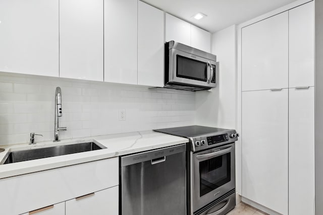 kitchen with stainless steel appliances, sink, light stone countertops, white cabinets, and tasteful backsplash