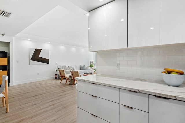 kitchen with light hardwood / wood-style floors, tasteful backsplash, light stone countertops, and white cabinets