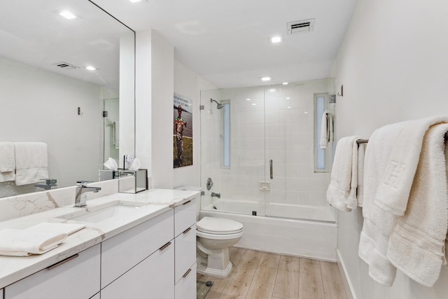 full bathroom with vanity, combined bath / shower with glass door, hardwood / wood-style flooring, and toilet